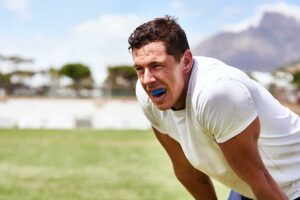 sweaty athlete bent over breathing hard showing off the mouthguard that is protecting his teeth and preventing sports related dental injuries