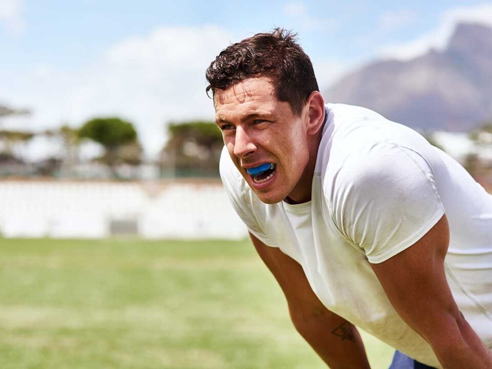 sweaty athlete bent over breathing hard showing off the mouthguard that is protecting his teeth and preventing sports related dental injuries