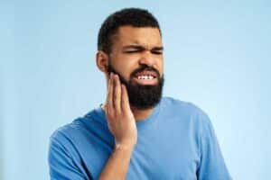 man with a big beard holds his face as an apparent toothache hits