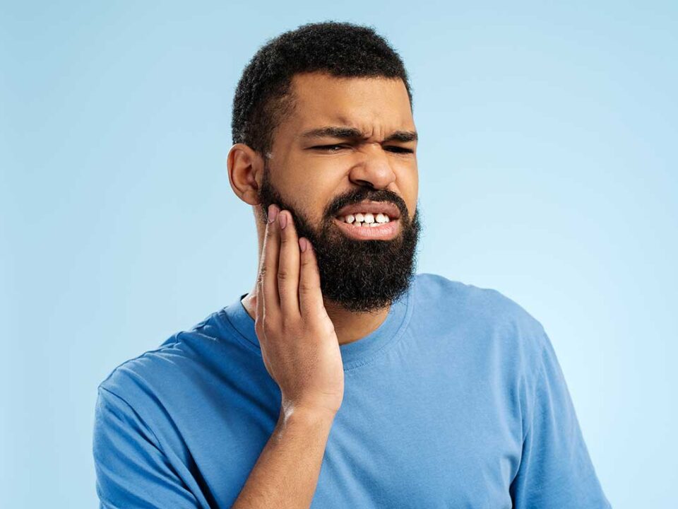 man with a big beard holds his face as an apparent toothache hits