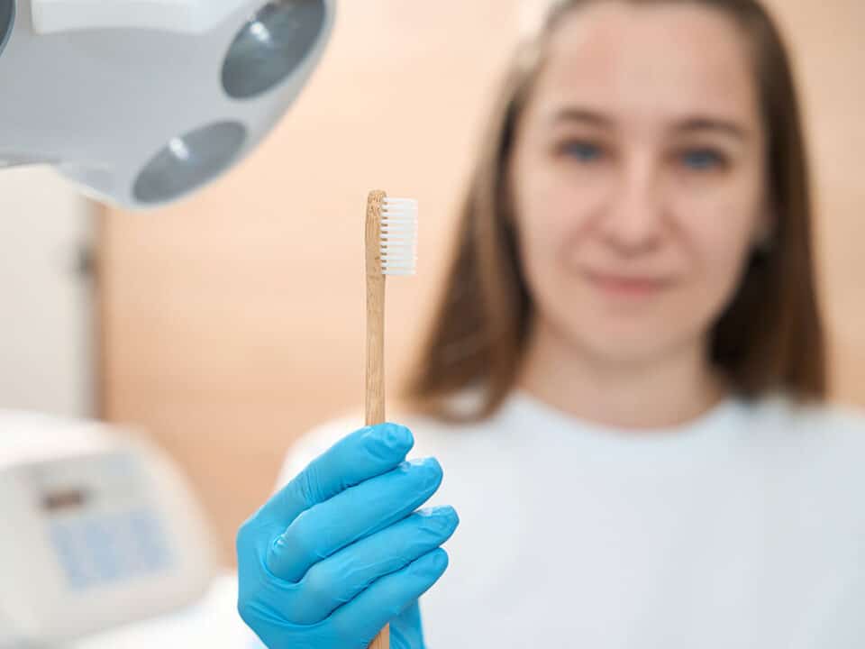 female dentist holds up a toothbrush as she tells you how often you should you replace your toothbrush