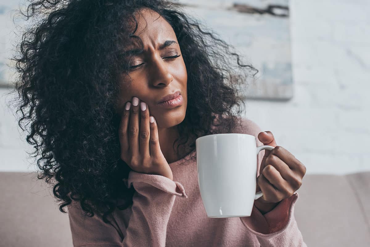 frizzy haired woman holds coffee mug of hot liquid that caused her to have a bout of tooth sensitivity pain 