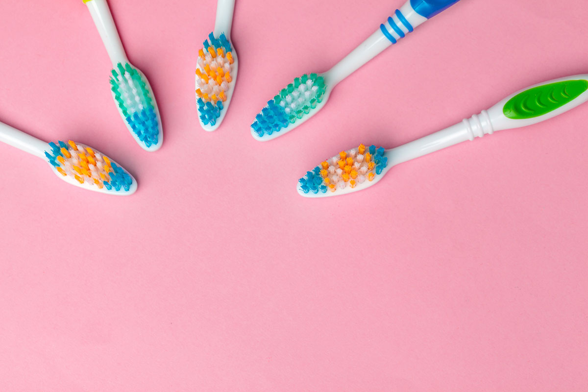 lineup of fresh toothbrushes on a pink background