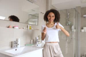 woman in her bathroom is holding a toothbrush and giving the thumbs up because she's using at home remedies for gum disease and they're working