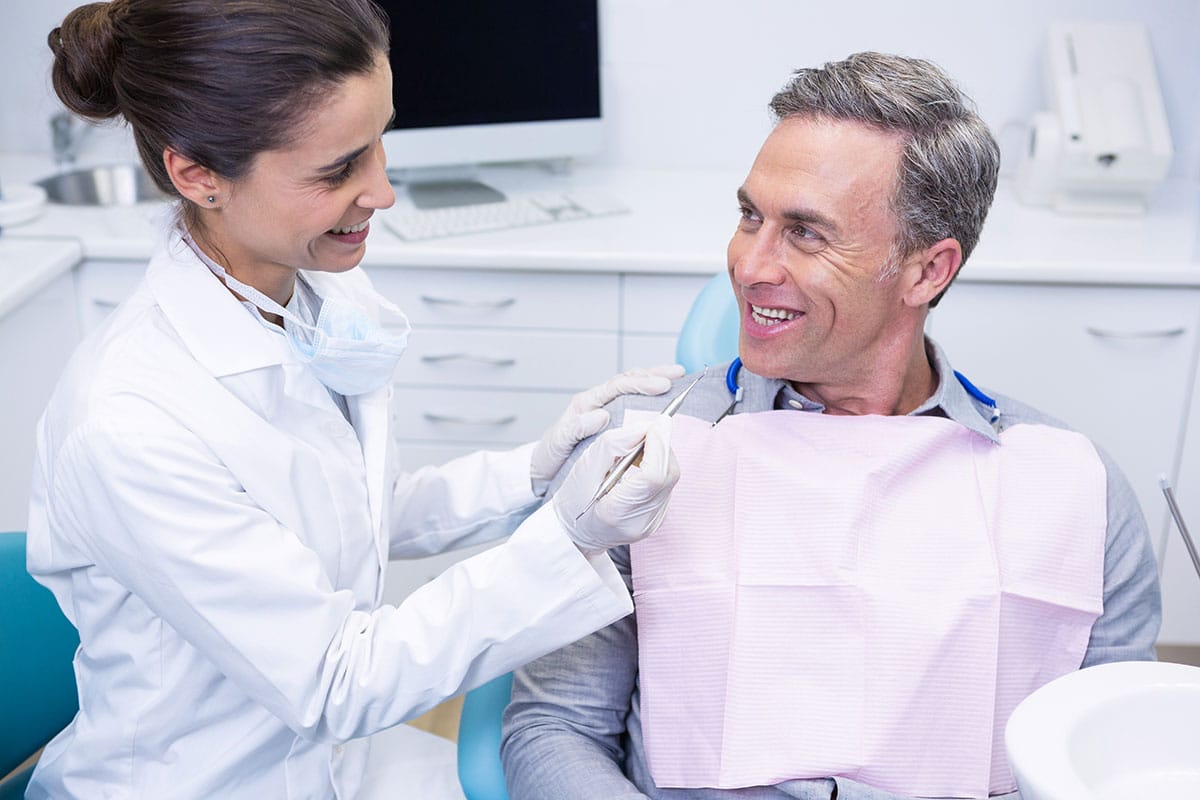 middle aged man smiles at his dentist as she attaches the bib around his neck