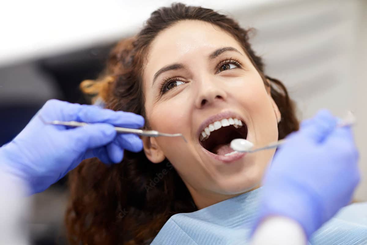 woman having her teeth cleaned at the dentist. she's smiling and has a purple bib on.