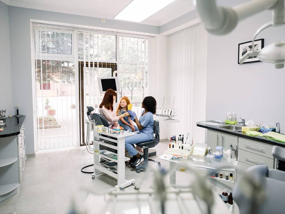 child with her mother in the dentists chair as the dentist answers the question do Dental Clinics Benefit from Offering CDCP Coverage