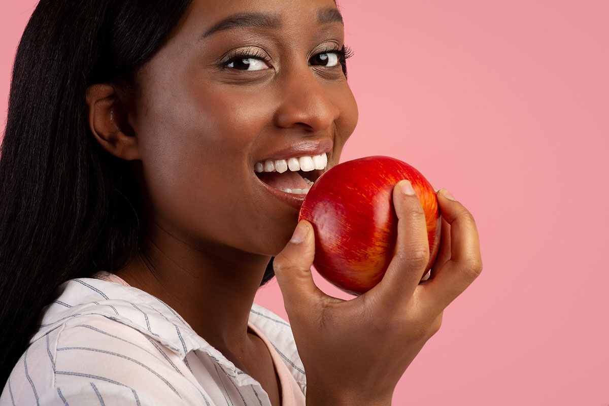 image showing an african woman about to eat an apple in front of a pink background