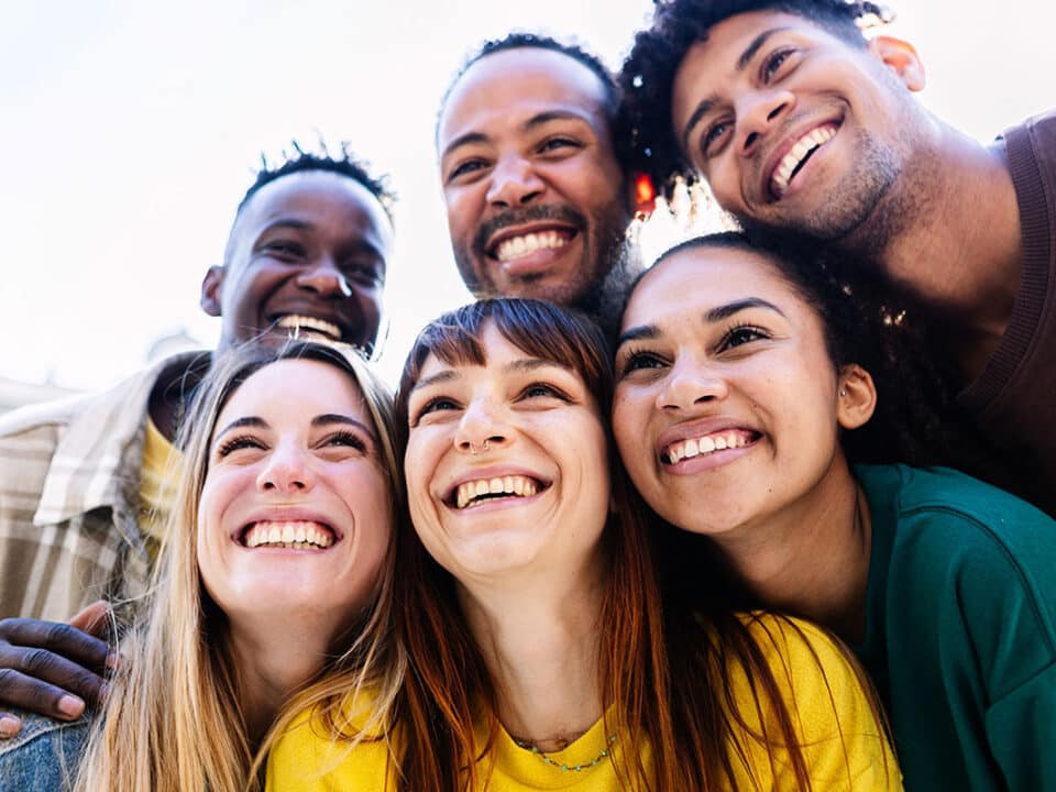 group of young adults clustered together and smiling at the camera. their teeth are perfect so they obviously know about the keys to preventing gum disease