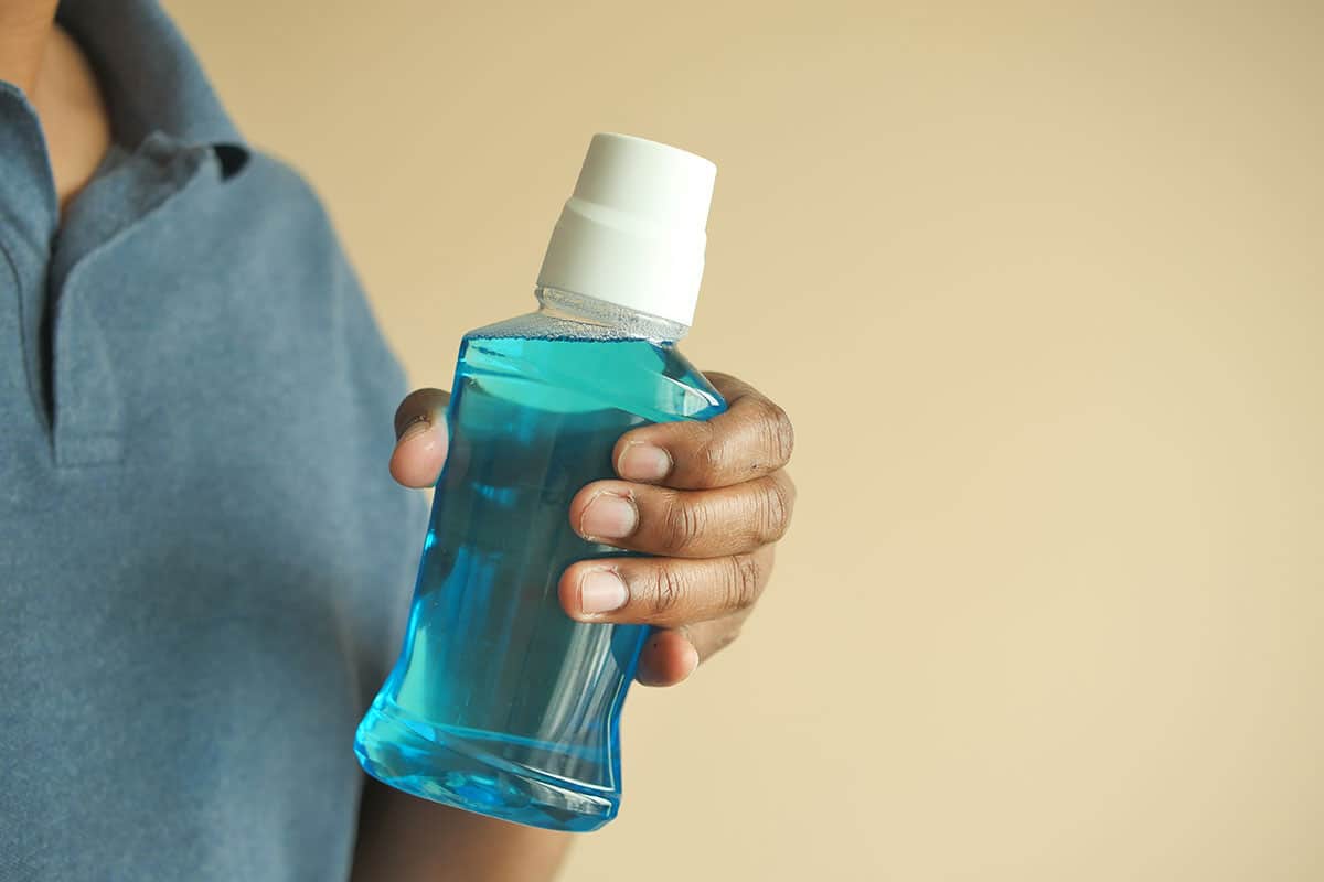 image of a hand holding a generic bottle of blue mouthwash on a beige background