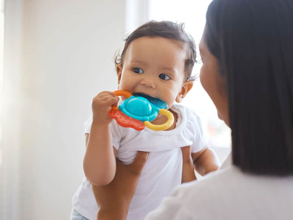 young baby is chewing on a teething ring as her mother wonders what to do if my child is teething.