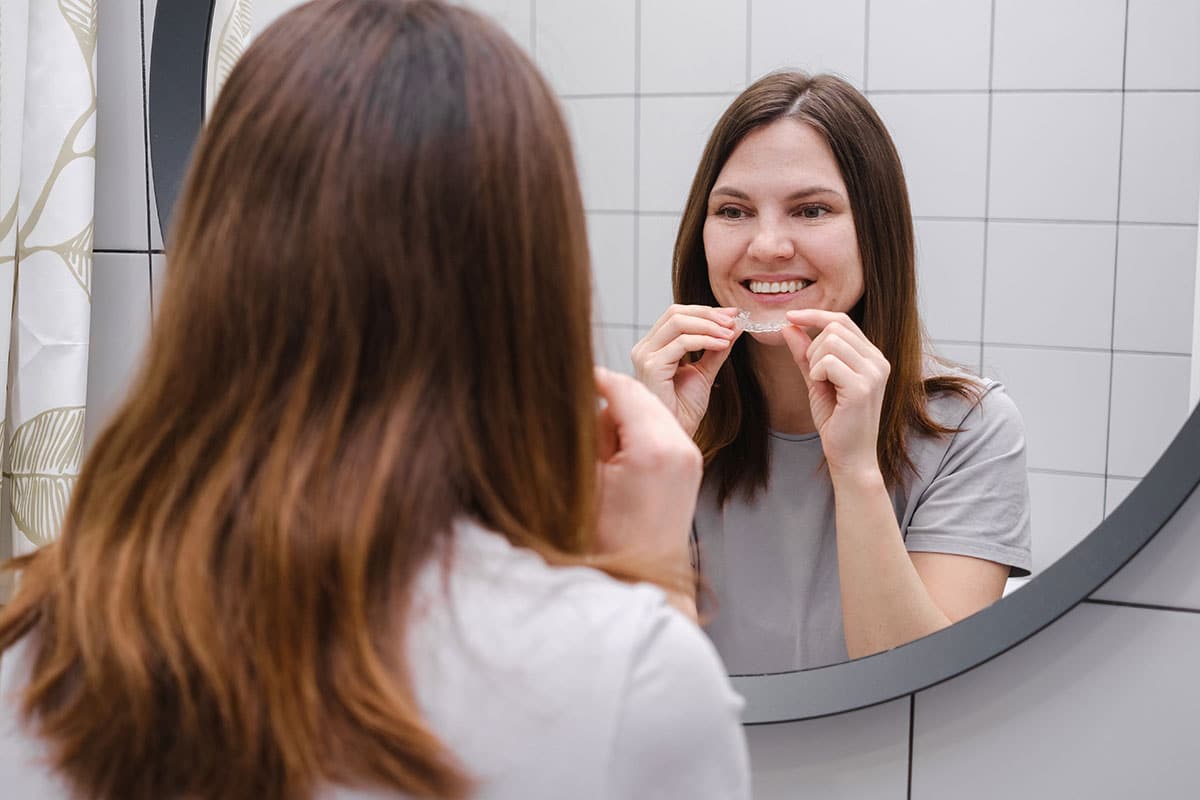 woman inserting a night mouth guard in her bathroom mirror