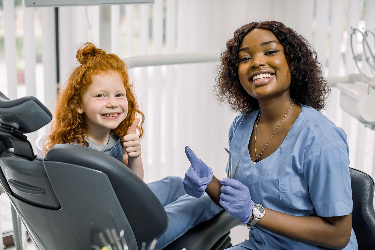 african dental hygienist sitting with a red haired child in the dentist chair making her feel at ease at the dentists office