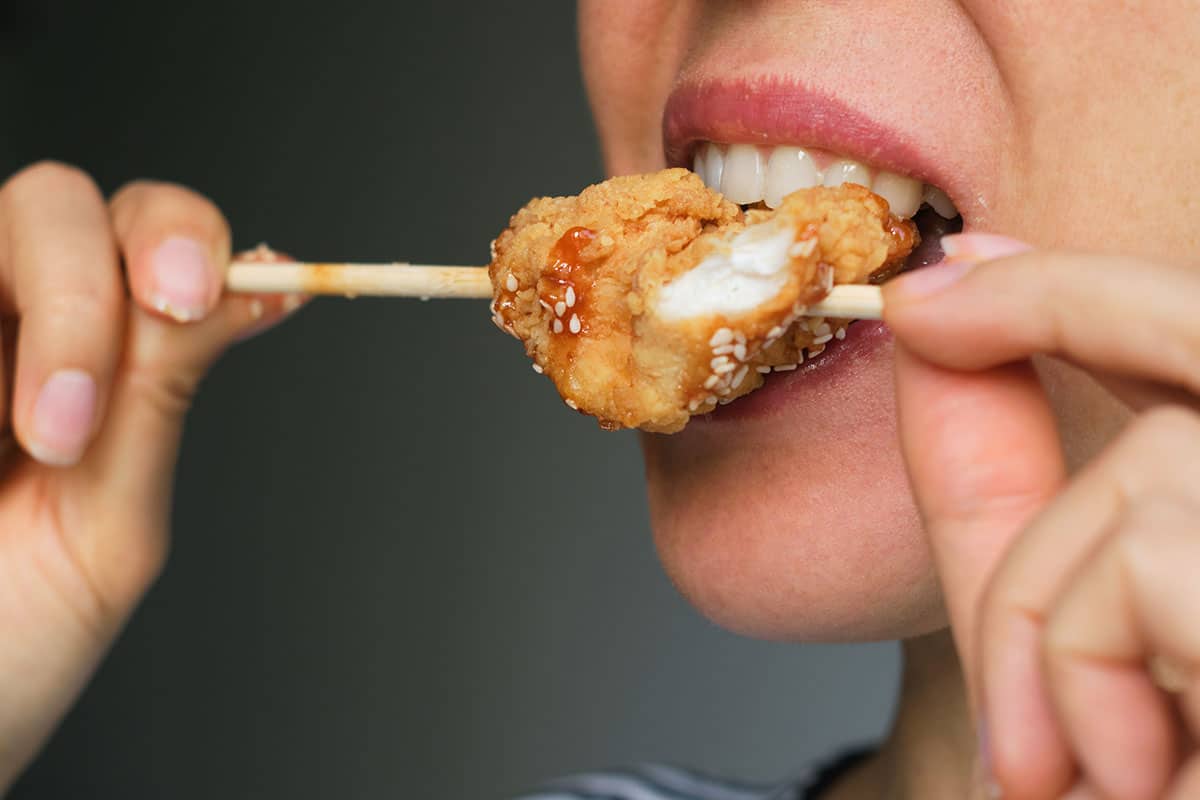 woman eating some fried chicken off a shiskabob stick