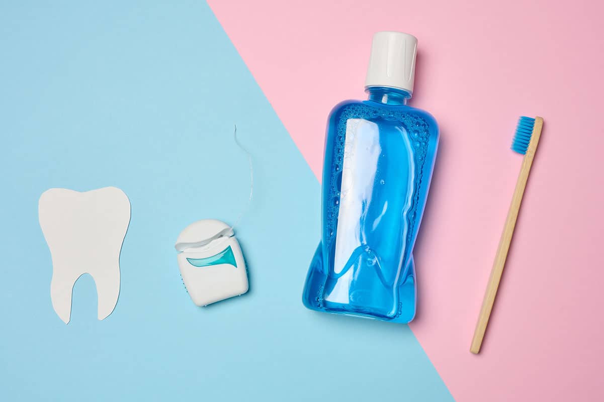 bottle of mouthwash and floss on a pink and blue background