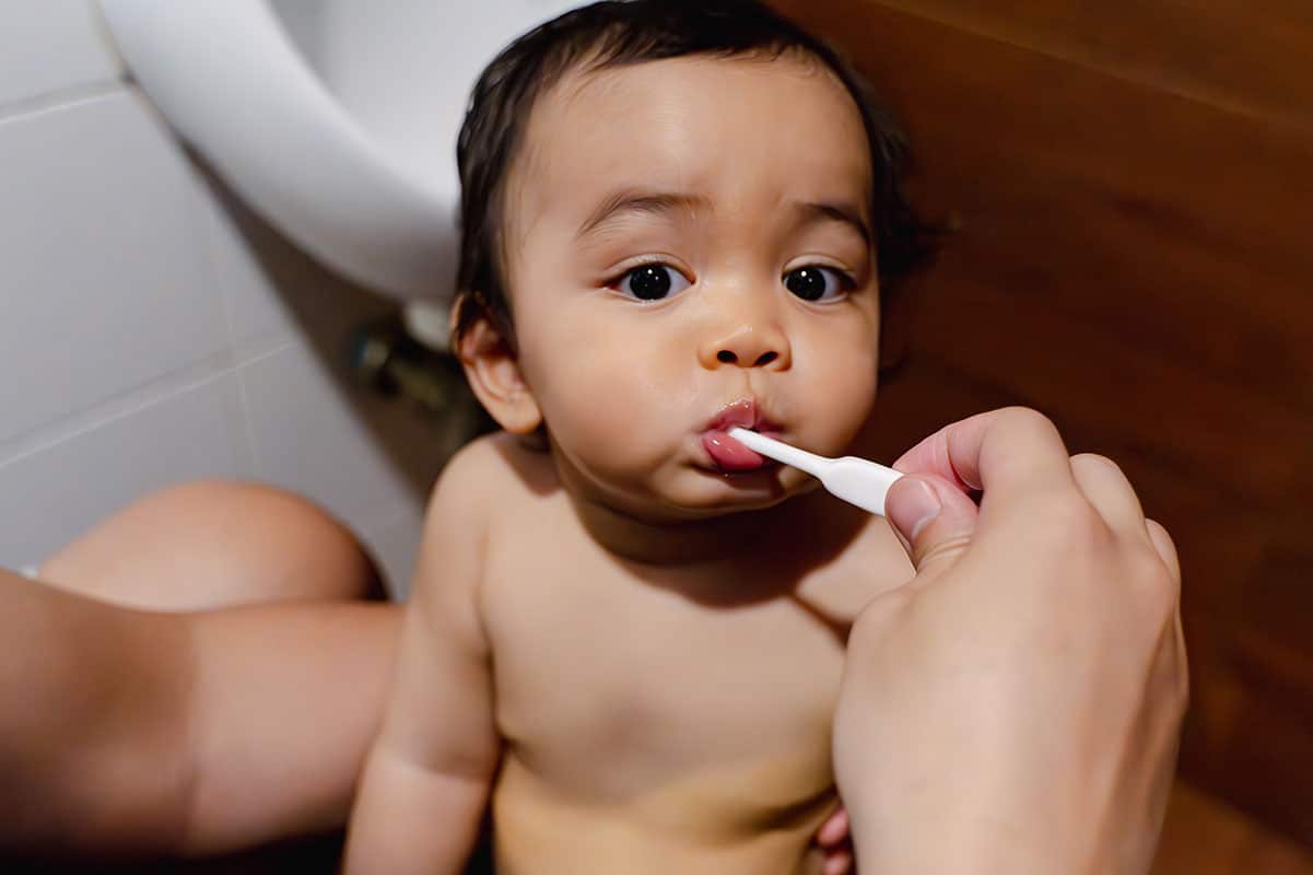 toddler with a toothbrush in his mouth learning how to brush his teeth