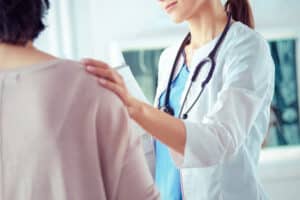 dentist has her hand on the shoulder of her patient as she explains the importance of oral cancer screenings