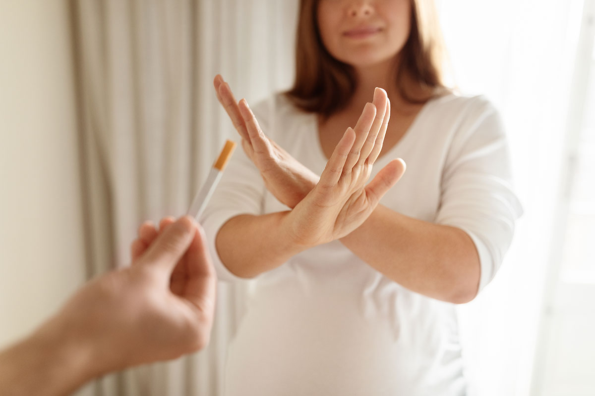 woman with her hands in an X shape saying no to a cigarette being offered by her friend