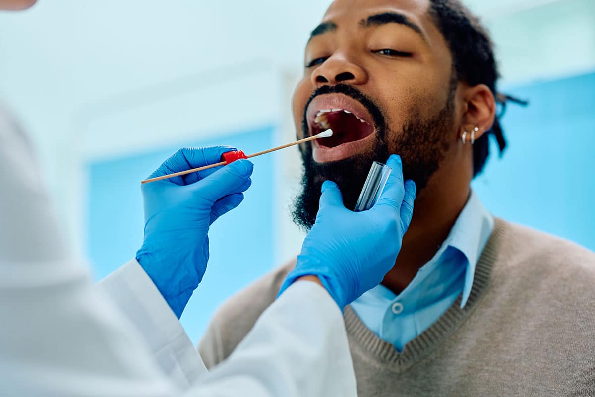 african man is getting a mouth swab to check for oral cancer as part of a routine biopsy at his dental office