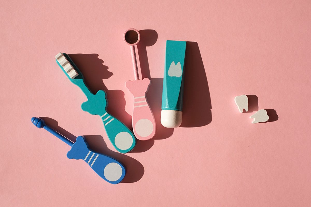 a set of wooden teeth cleaning tools like toothbrush, toothpaste and a mirror are laid out on a pink background