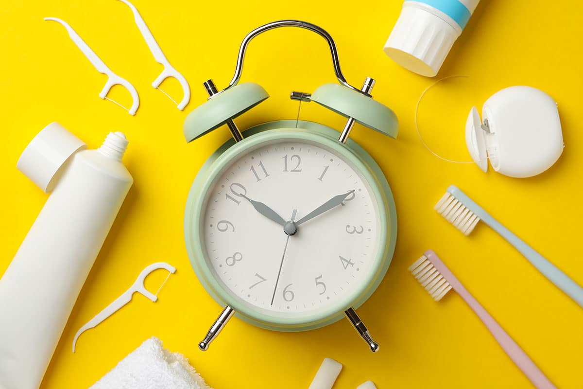 analog clock surrounded by dental care tools on yellow background