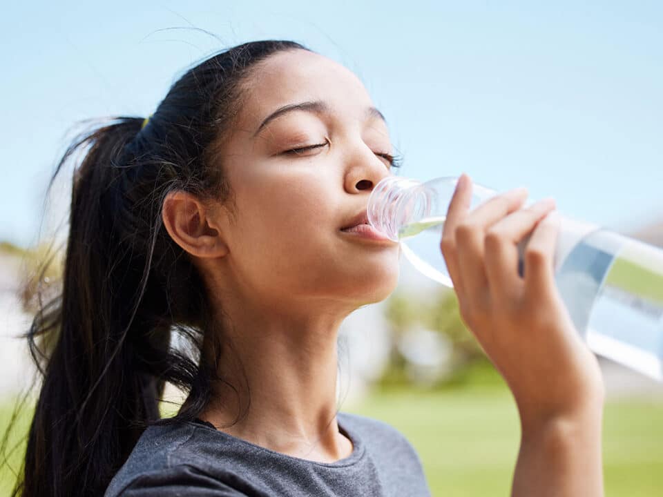 young woman drinking from a bottle of water as one of the many dry mouth solutions and treatments options