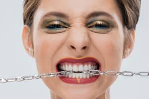 woman shows off her strong teeth by biting on a steel chain as the Top 10 Foods That Strengthen Teeth Naturally hero image