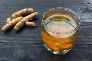 a piece of raw ginger sits on a cutting board beside a brewed cup of tea as one of the fifteen mentioned natural toothache remedies