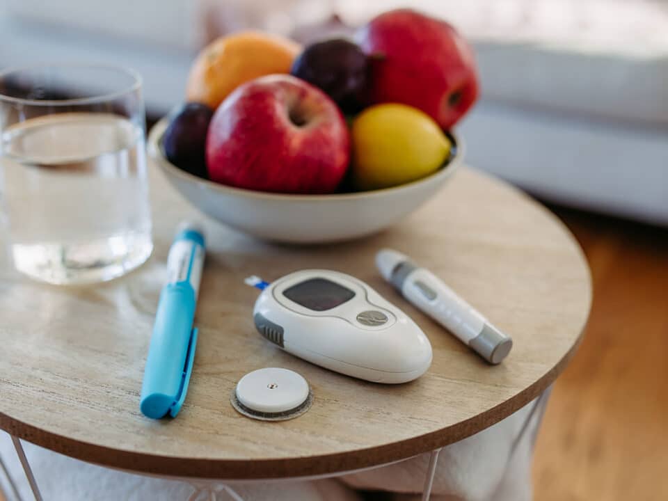 featured image of the diabetes and oral health article shows an insulin needle, a blood sugar monitor and some fruit on a table