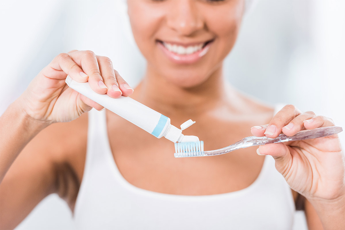 iamge showing a woman squeezing some toothpaste onto her toothbrush as she smiles.