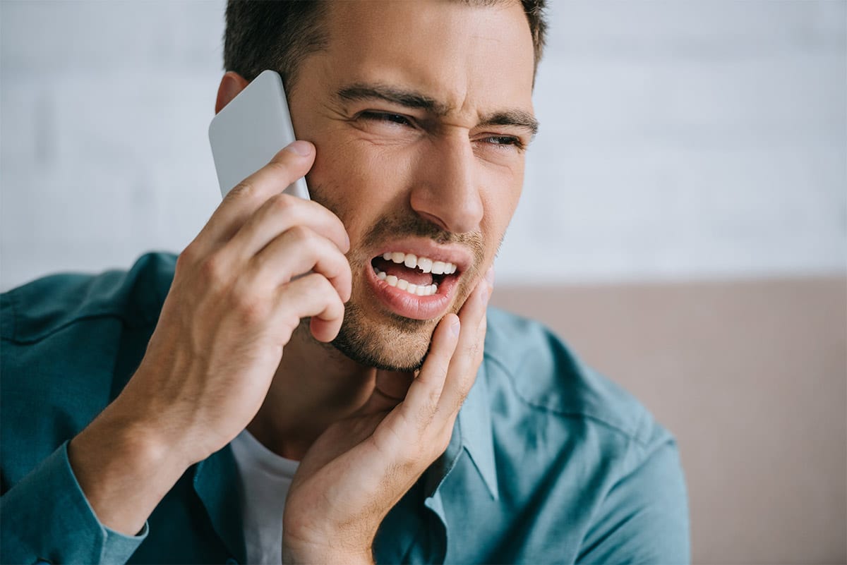 man with a chipped tooth is on the phone calling his dentist for treatment advice and an appointment