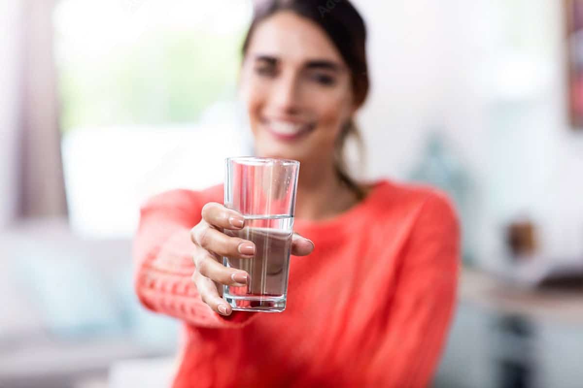 woman in a red sweater holds out a glass of water as a suggestion on how to boost saliva production