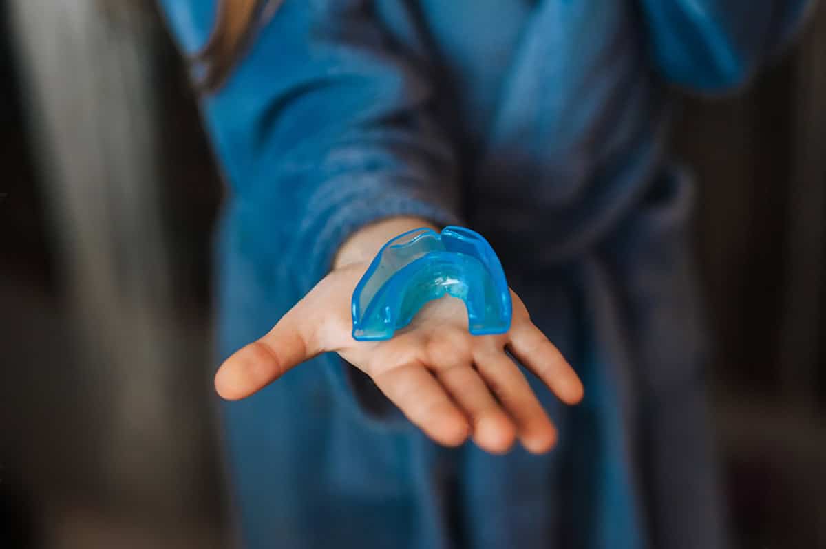 woman dressed in blue holds out a moutguard which is used for preventing chipped or cracked teeth