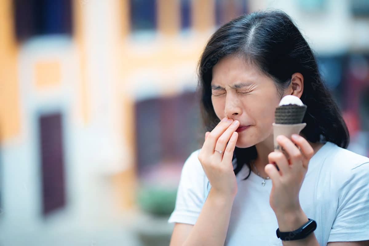 asian woman clutches her mouth as her sensitive teeth react to the cold ice cream cone she's eating