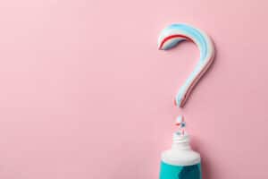featured image for how to choose the right toothpaste which shows a tube of toothpaste with a question mark spelled out in paste on a pink background