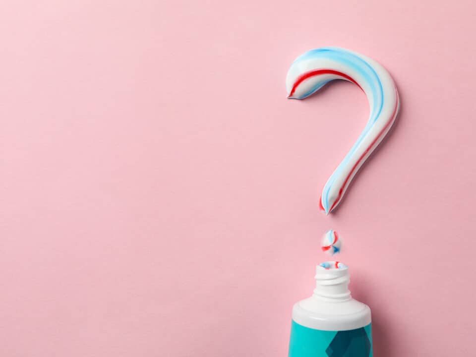 featured image for how to choose the right toothpaste which shows a tube of toothpaste with a question mark spelled out in paste on a pink background