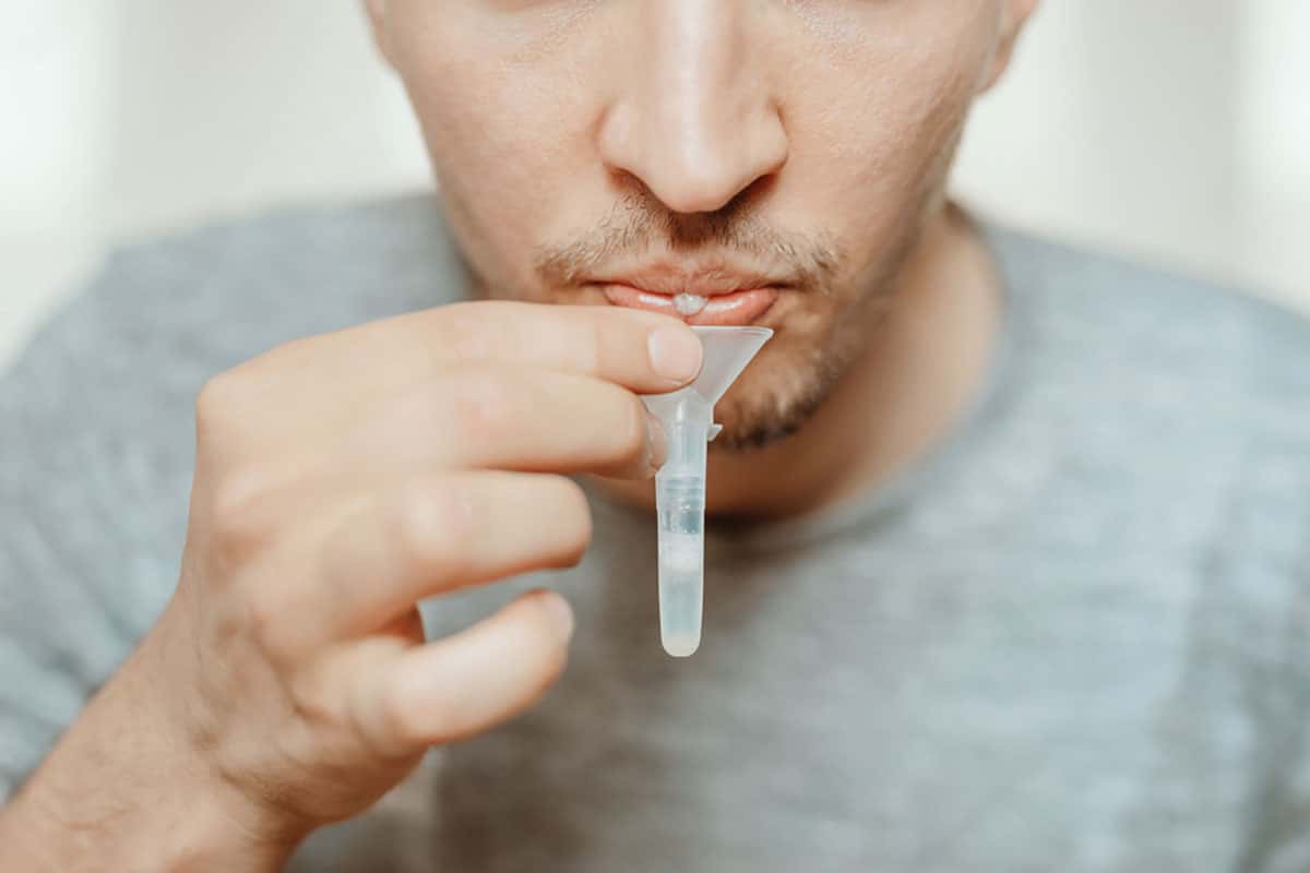 man spits saliva into a test tube as the what is saliva header image
