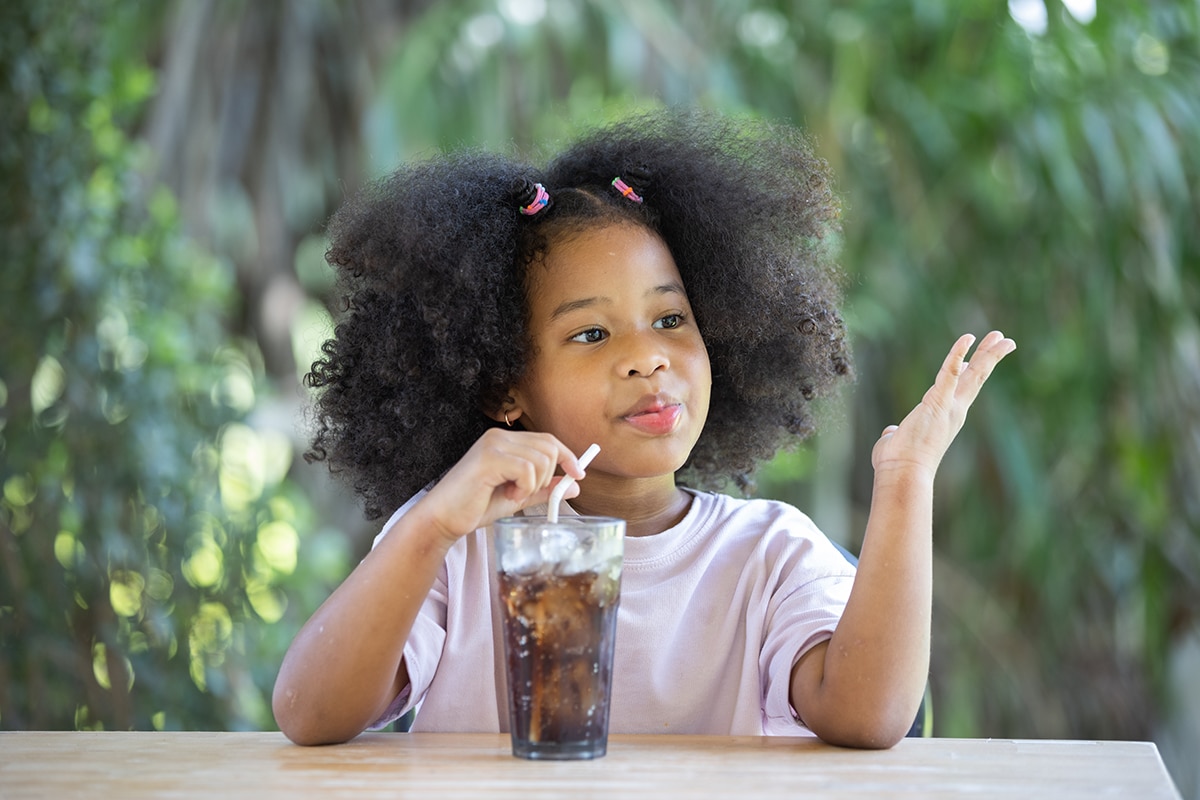 young girl drinking a coca cola soda out of a glass which isn't great nutrition for dental milestones (if you ask her dentist)