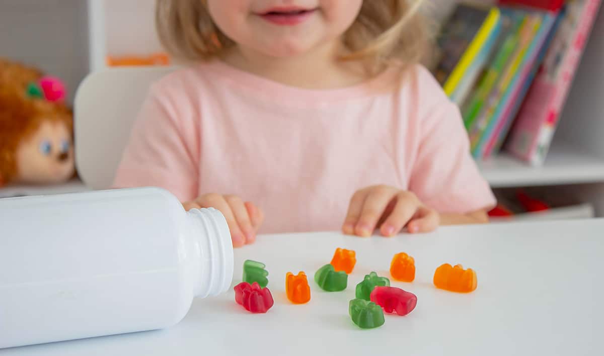 little girl about to eat some gummies that are strewn on the table in front of her.