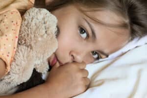 photo shows a young girl holding her teddy bear while sucking her thumb as she wonders how to stop thumb sucking