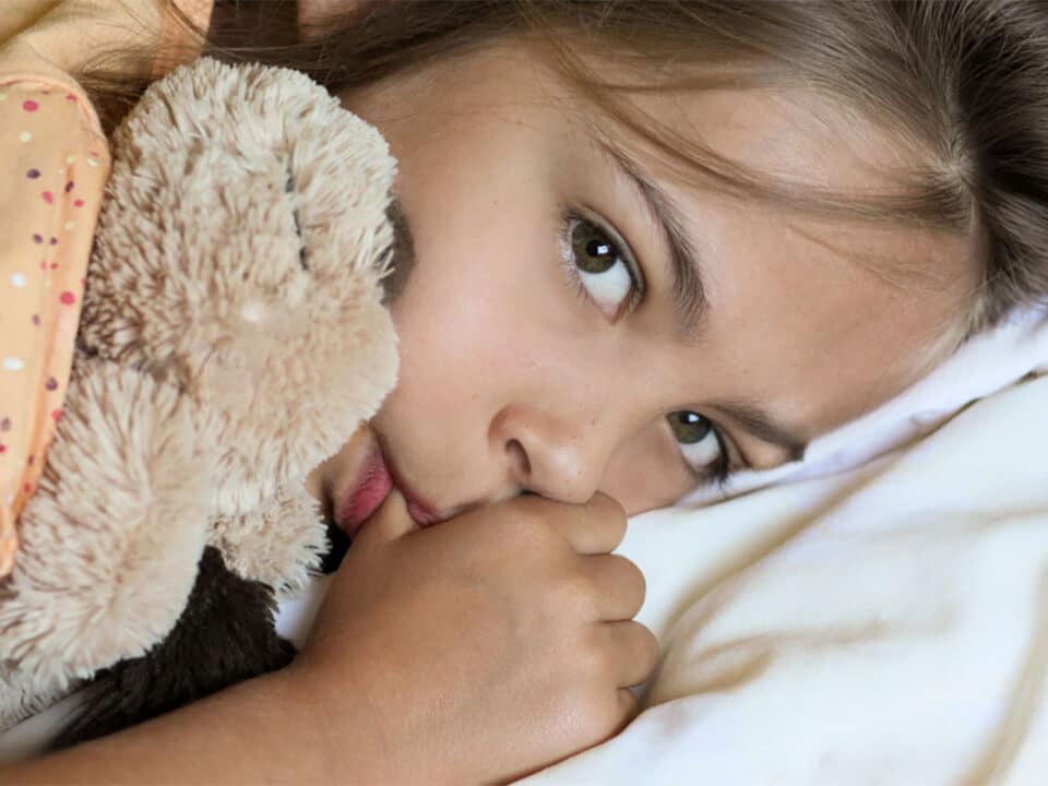 photo shows a young girl holding her teddy bear while sucking her thumb as she wonders how to stop thumb sucking