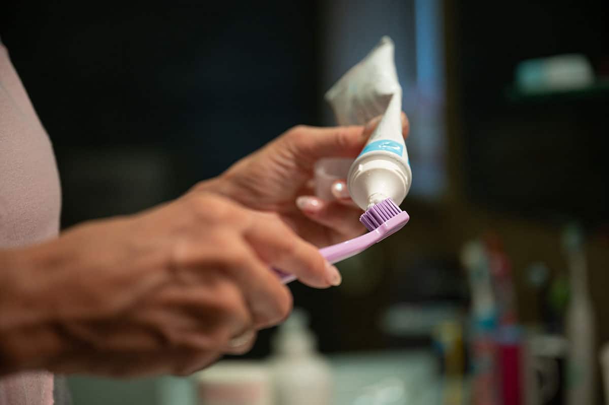 woman applying sensitivity toothpaste onto her pink toothbrush