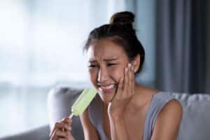 asian woman hit by tooth pain while eating a popsicle, so she wonders "why are my teeth sensitive?"