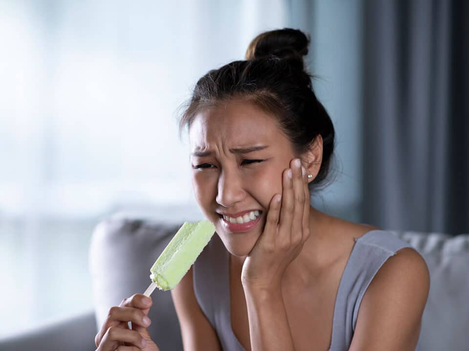 asian woman hit by tooth pain while eating a popsicle, so she wonders "why are my teeth sensitive?"