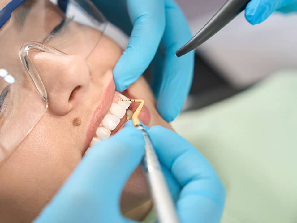 woman with safety glasses on is having her teeth deep cleaned b her dentist after reading up on deep dental cleanings vs regular cleanings and making the decision to go for it