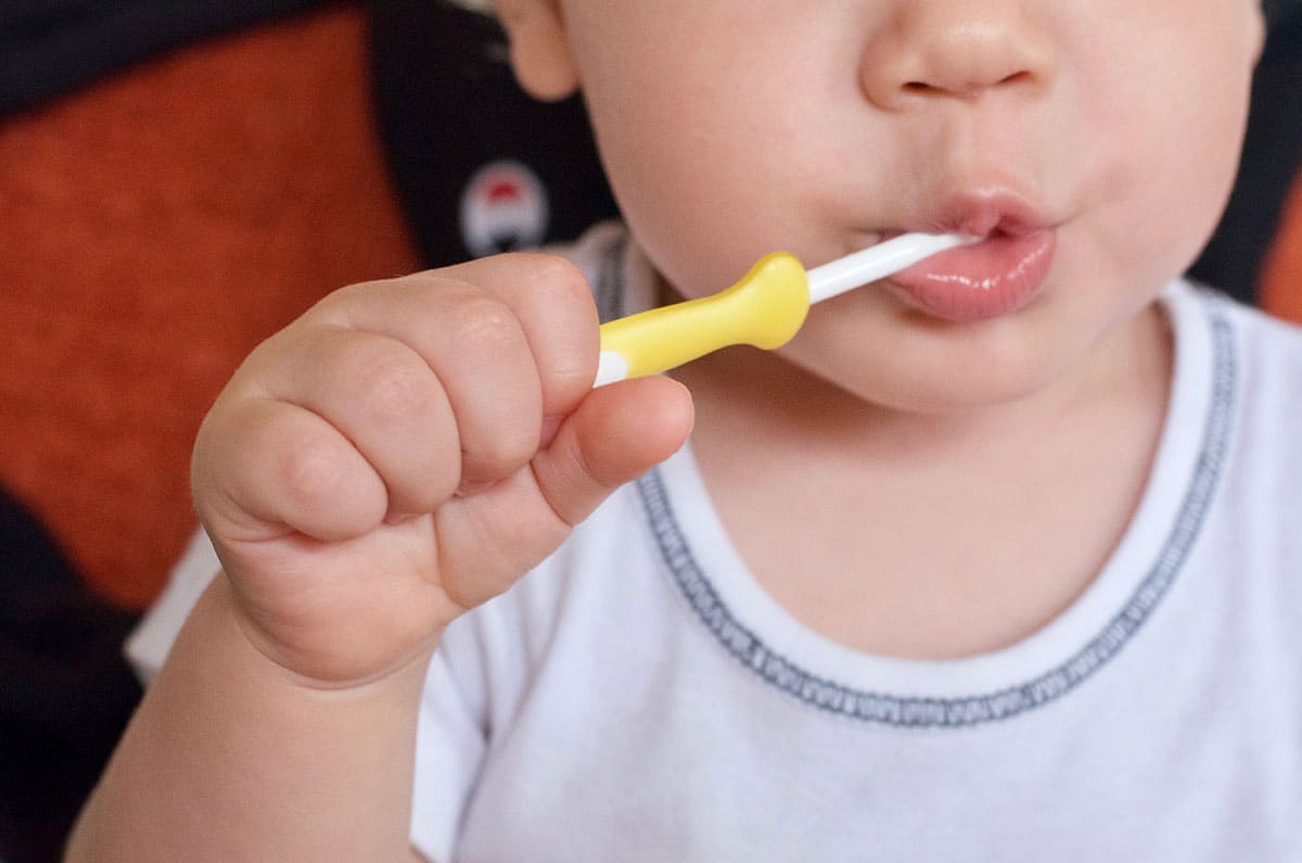 young toddler is experimenting with brushing teeth under mommy's supervision