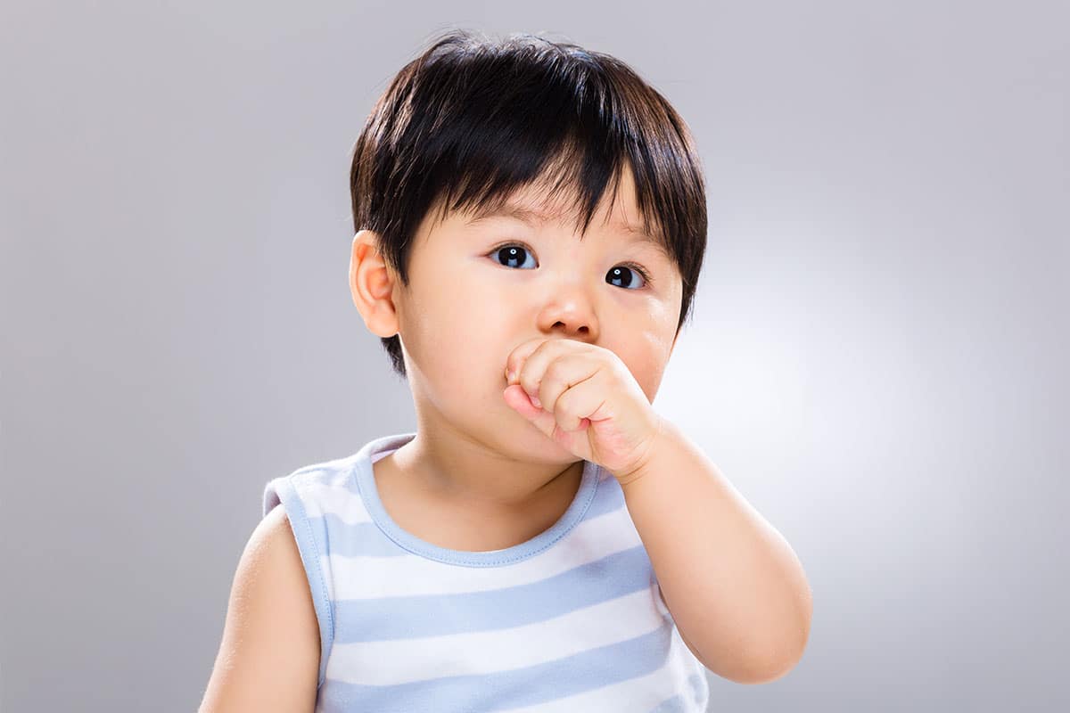 small Asian toddler sucks his thumb while looking pensively at the camera