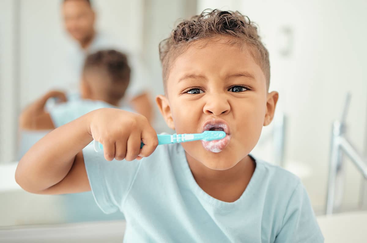 young boy wearing a blue shirt does a great job brushing his teeth in the bathroom mirror