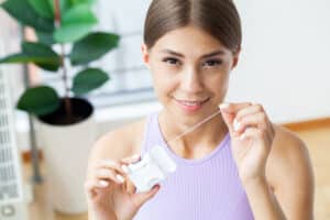 woman smiling as she holds a container of floss and debates - floss vs waterpik, which is better?