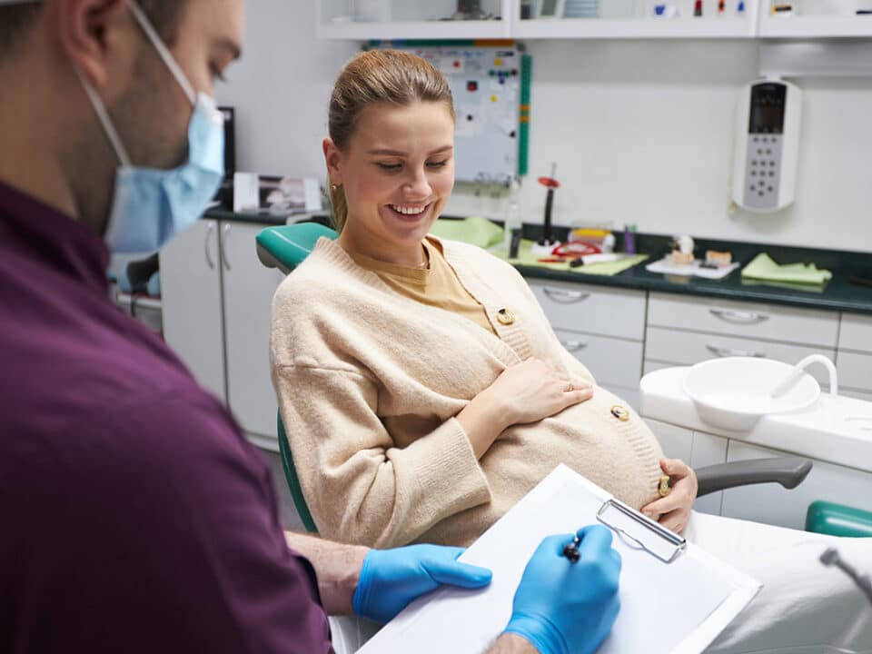 pregnant woman is sitting in the dentist chair speaking with her dentist about managing gum disease during pregnancy